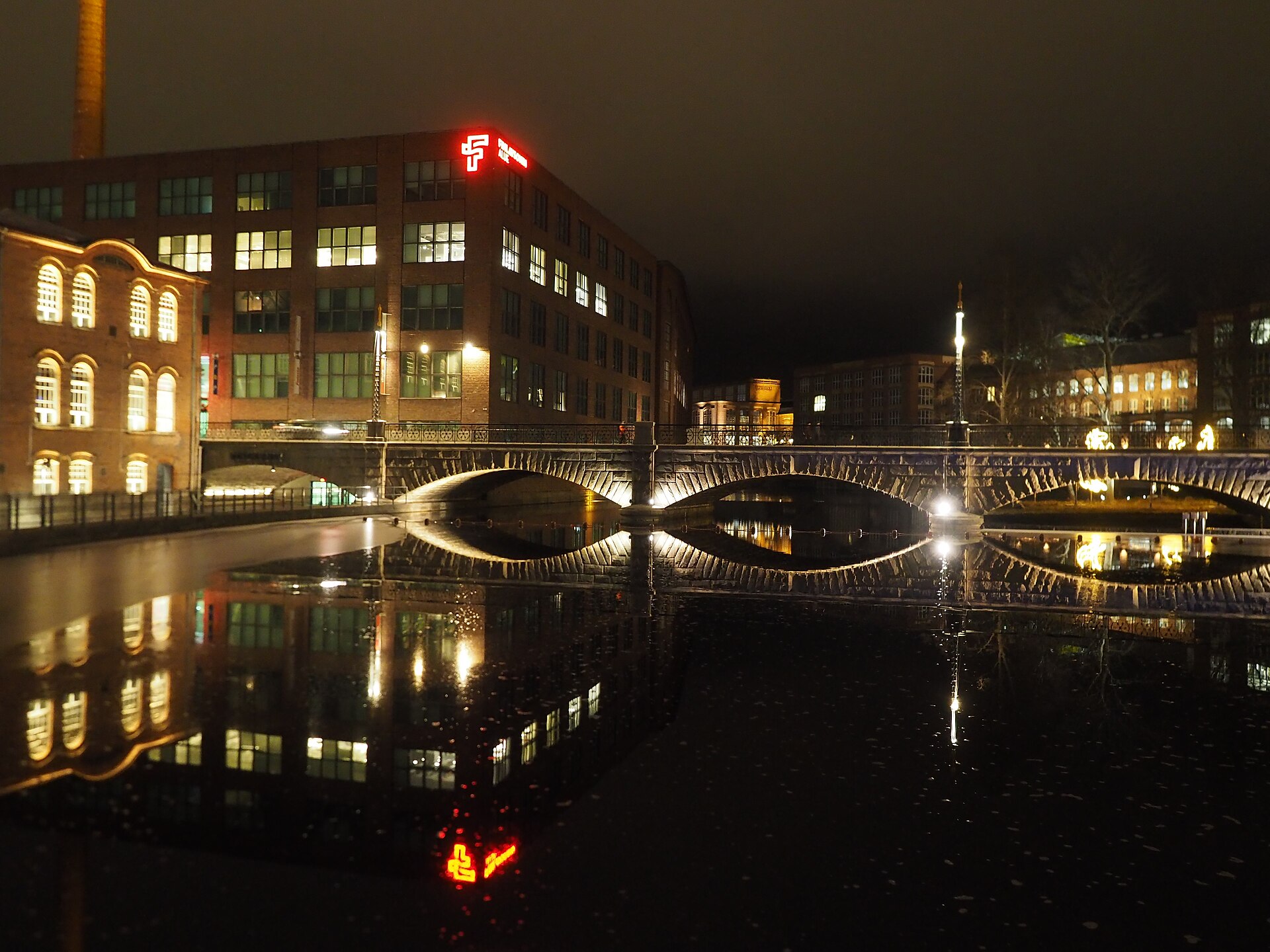 Night view across Tammerkoski in Tampere with lit bridge and industrial buildings reflected in the water