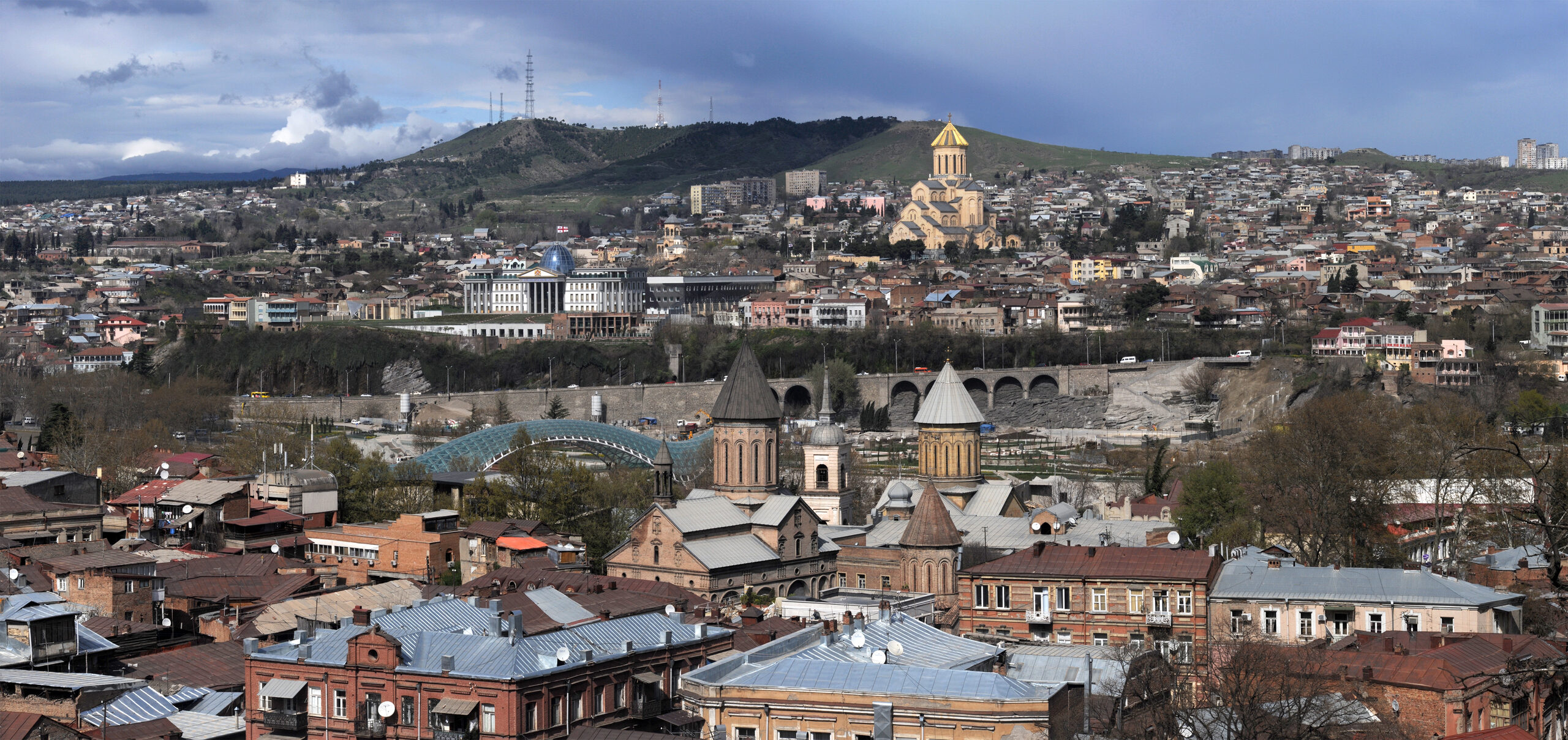 Wide Tbilisi panorama with city rooftops, churches, hills, and the river valley