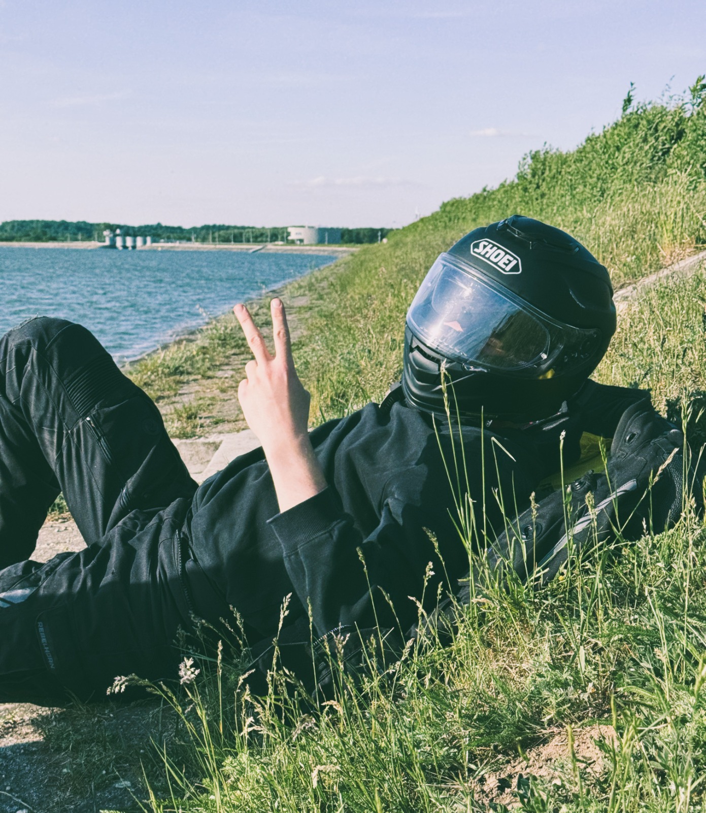 Rider in motorcycle gear taking a break beside a lakeside embankment